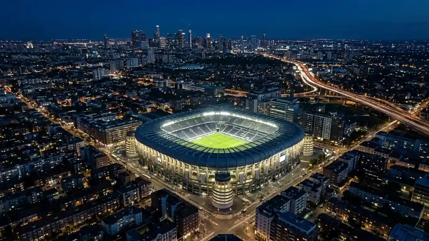 Vue aérienne nocturne d'un grand stade illuminé au milieu d'une ville, silhouettes de gratte-ciel au loin