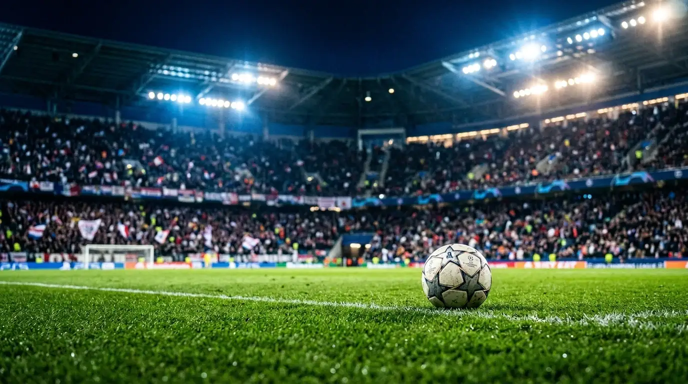 Ballon de football posé sur la pelouse d'un stade illuminé la nuit, tribunes floues remplies de supporters, ambiance de match décisif